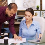 Young female architect working on laptop and talking with chief constructor