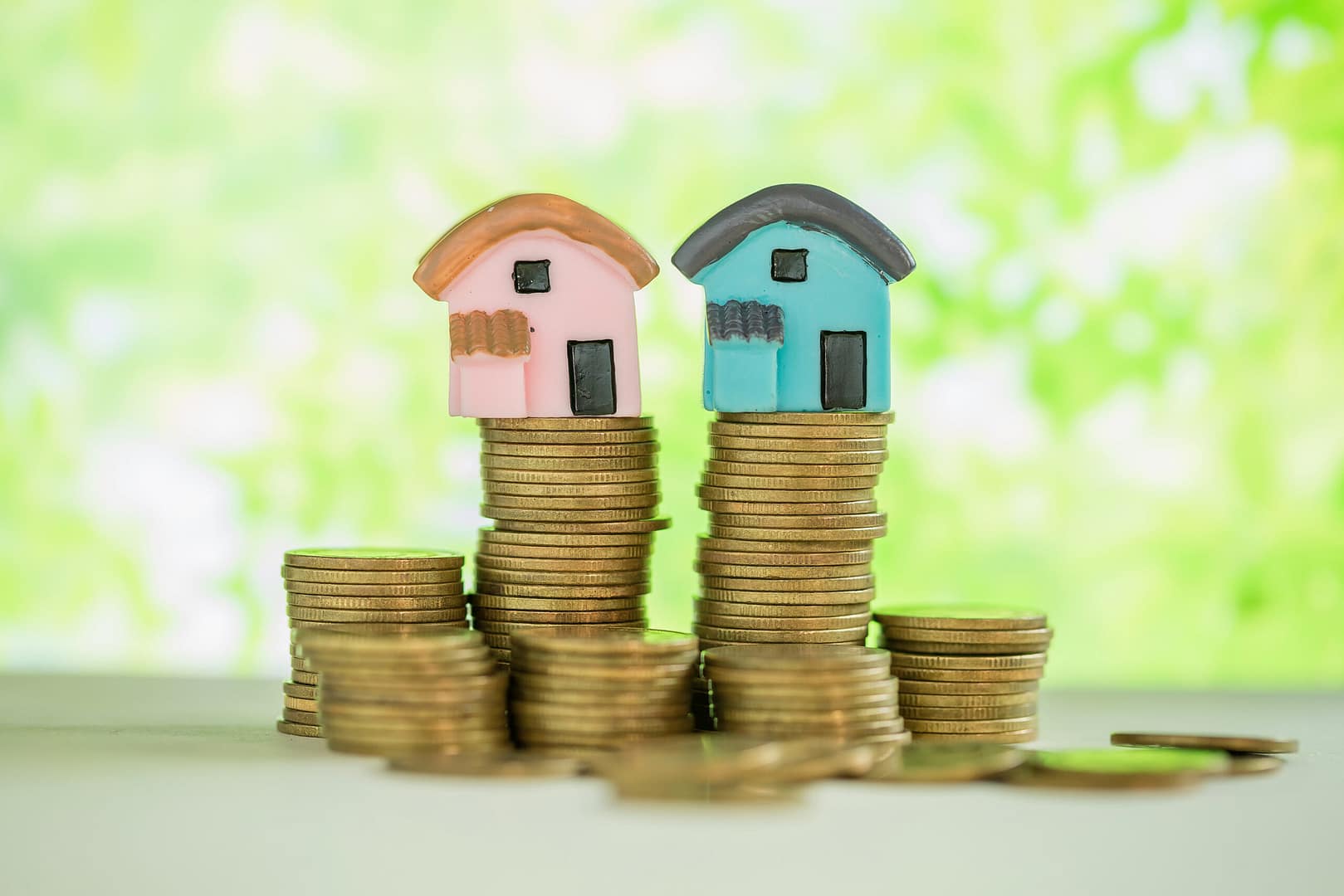 Mini house on stack of coins with green blur background.